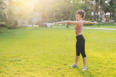 Sağlıklı açık hava yaşam tarzı 30 'lu yaşlardaki genç Asyalı kadınlara pembe spor kıyafetleri giydirip koşudan önce parkta vücut ısıtma egzersizleri hazırlıyor. Günbatımında fitness koşucusu kız. Refah ve refah kavramı.