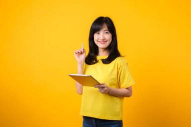 Eğitim teknolojisinin zevkini portre ile yaşayın. Sarı tişört ve kot pantolon giyen Asyalı genç bir kadın dijital tablet kullanırken mutlu bir gülümseme sergiliyor. eğitim teknolojisi kavramı.