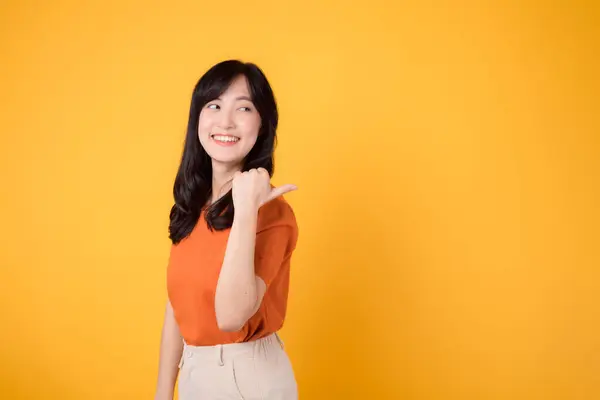 和一位30多岁的年轻亚洲女人一起庆祝快乐 穿着橙色的衬衫 用她的大拇指指指着黄色背景的复制空间 产品推荐概念 — 图库照片
