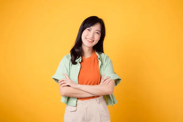 与身穿橙色衬衫的30多岁的亚洲女人一起 释放出自信和幸福的力量 她的胳膊在黄色的背景下交叉地放在胸前 流露出自信和内心的平静 — 图库照片