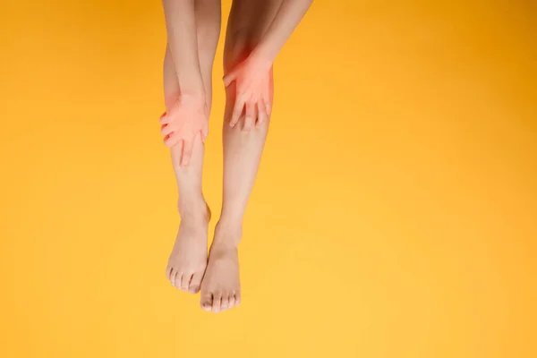 A close up of woman\'s legs with hands holding their pained legs on vibrant yellow background. Embodying the concept of legs healthcare.