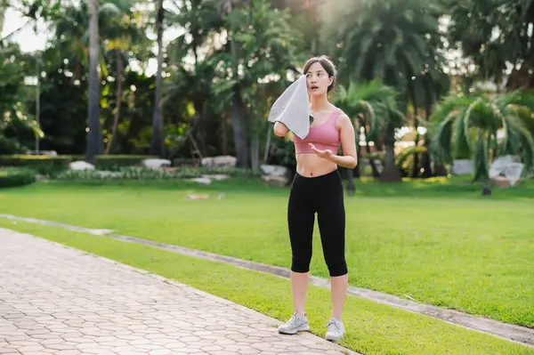 在公园里跑了一上午之后 身穿粉色运动服的30多岁的亚洲女人擦拭着自己的脸颊 拥抱健康生活方式的美丽 达到健身目标 并有成就感 — 图库照片