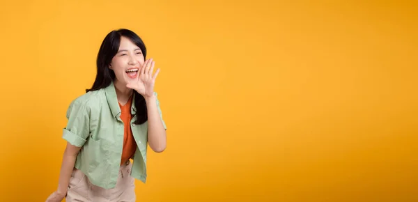緑とオレンジ色のシャツを着た活気のある若いアジアの女性30代は 黄色の背景に隔離された彼女の口で精力的に叫びます ディスカウントショッピングプロモーションのコンセプトを探る — ストック写真