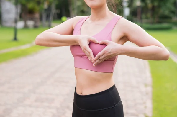 Woman jogger. asian young female happy smile wearing pink sportswear showing heart hands gesture on chest before running in public park. Healthcare wellness concept.