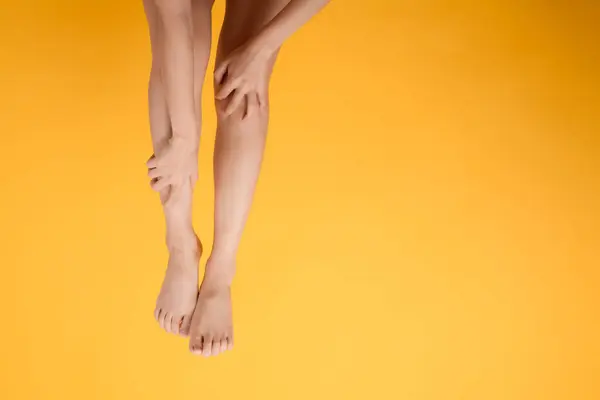 Explore legs healthcare with close up of woman\'s legs, hands holding her pained legs on a vibrant yellow background. Concept of leg pain relief.