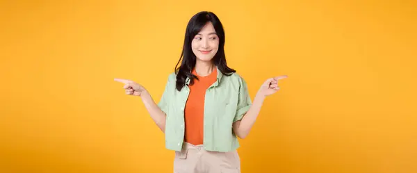 best deal promotion concept featuring young 30s Asian woman, wearing green shirt on orange shirt. With happy face, points her finger to free copy space, choose deals offers against yellow backdrop.