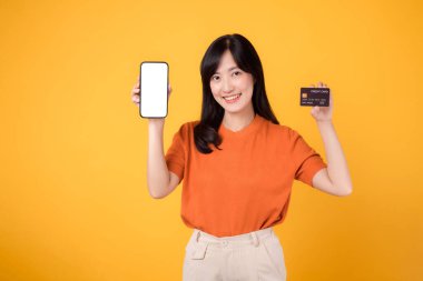 Enerjik 30 'lu yaşlarda Asyalı bir kadın, parlak sarı arka planda akıllı telefon ve kredi kartı gösteriyor. Kusursuz online ödeme alışverişi