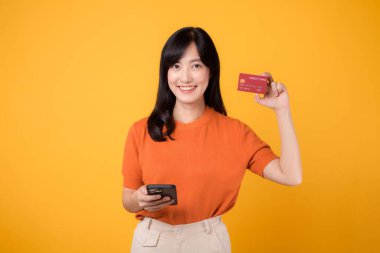 30 'lu yaşlarda Asyalı heyecanlı bir kadın, akıllı telefon kullanıyor ve sarı arka planda kredi kartı gösteriyor. Kullanışlı online alışveriş