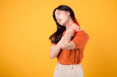 Otuzlarında, turuncu gömlek giyen empatik genç Asyalı kadın sarı arka planda ağrılı boynunu tutuyor. ofis sendromu sağlık hizmeti kavramı.