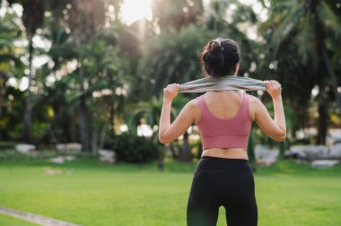 Halka açık bir parkta gün batımı koşusundan sonra ısınan 30 'lu yaşlarda, pembe spor giysili, mutlu ve formda bir Asyalı kadın. Sağlıklı yaşamı ve doğanın güzelliğini kucakla..