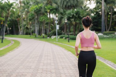 Kadın koşucu. Kamu parkında koşan pembe spor giysili Asyalı genç bir kadının arka perspektif portresi. Sağlık hizmetleri sağlık konsepti.