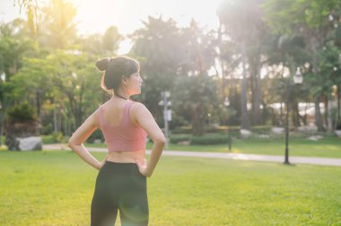 Doğada mutlu, formda, 30 'lu yaşlarda bir Asyalı kadın olarak gün batımından önce vücudunu halka açık bir parkta, pembe spor kıyafetleriyle ısıtırken sıhhatini kucaklayın..