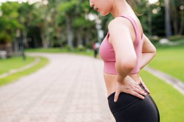 Kadın koşucu. 30 'lu yaşlarda genç Asyalı kadın parkta koştuktan sonra sırtını kolluyor ve kalçasında ağrı var. Etkinlik konseptinde acı.