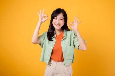 Turuncu gömlek ve yeşil kazak giymiş 30 'lu yaşlardaki hoş Asyalı kadın. Onun etkileyici el hareketi ve nazik gülümsemesi sarı arka planda parlıyor, vücut dili kavramında..