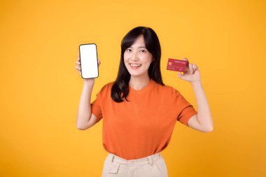 30 'lu yaşlarda canlı bir Asyalı kadın, sarı arka planda akıllı telefon ve kredi kartı sergiliyor. Çevrimiçi ödeme alışverişi zahmetsiz.
