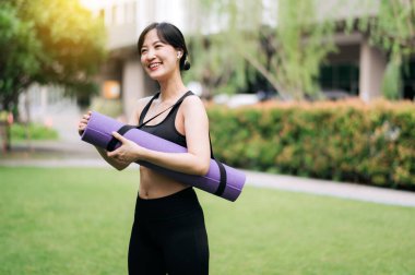 Kauçuk bir hasırla, Asyalı kadın gün batımında parkta egzersiz için hazır bekliyor. Fitness, doğa ve sağlıklı bir yaşam tarzını kucaklamak.