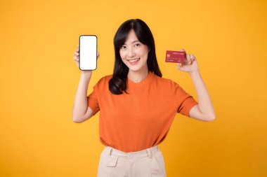 30 'lu yaşlarda tutkulu Asyalı bir kadın, sarı arka planda akıllı telefon ve kredi kartı sunuyor. Çevrimiçi hızlı ödeme alışverişi.