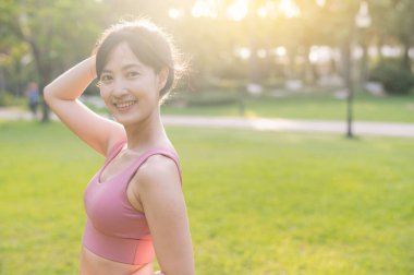 Mutlu bayan koşucu. 30 'larında güzel Asyalı bir kadın kameraya bakıyor ve gün batımında parkta gülümsüyor. sağlıklı yaşam konsepti.