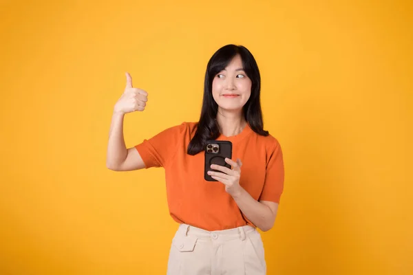 Energiczna Azjatka Trzydziestce Ubrana Pomarańczową Koszulę Używająca Smartfona Kciukiem Góry — Zdjęcie stockowe