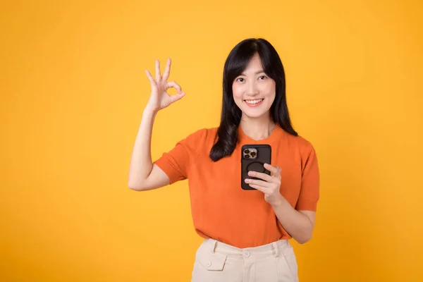Lächelnde Asiatin Die Orangefarbenes Hemd Smartphone Mit Handzeichen Auf Leuchtend — Stockfoto