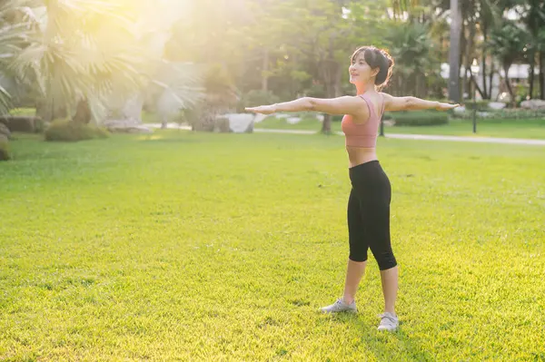 女性ジョギング ピンクのスポーツウェアで30代の若いアジア人女性にフィットして 走る前に公園で体を温めます 日没のフィットネスランナーガールとの健康的な屋外ライフスタイル 健康と福祉のコンセプト — ストック写真