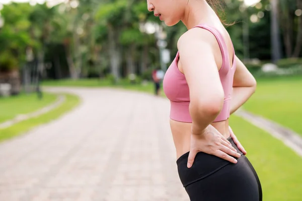 女慢跑者 三十来岁的年轻亚洲女子穿着粉色运动服 在公园里跑步锻炼 腰酸背痛 髋关节酸痛 活动中的疼痛概念 — 图库照片