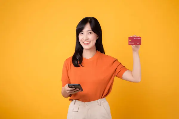 Radosna Azjatka Trzydziestce Używająca Smartfona Pokazująca Kartę Kredytową Żółtym Tle — Zdjęcie stockowe