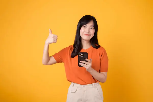 Веселая Азиатка Лет Одета Оранжевую Рубашку Использует Смартфон Большим Пальцем — стоковое фото