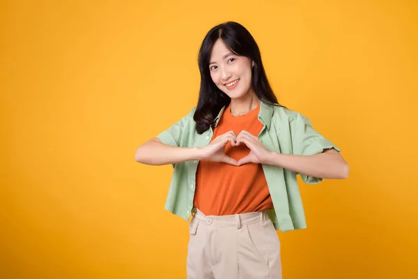 healthcare and wellness with an 30s Asian woman, wearing a green shirt. Witness her heart hand gesture on her chest against a yellow background, truly embracing the embodiment of body wellness.