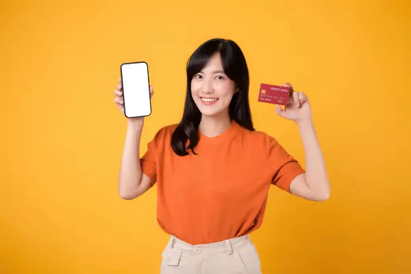 陽気なアジアの女性30代 黄色の背景にスマートフォンとクレジットカードを明らかに スムーズなオンライン決済ショッピング — ストック写真