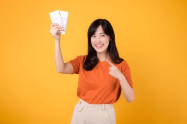 30 'lu yaşlardaki dinamik Asyalı kadın canlı sarı arka planda nakit para parasına işaret ediyor. Zenginlik ve refah kavramı.