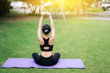 Portre 30 'lu yaşlarda, yoga minderli pembe spor giysili bir Asyalı kadına uydu. Parkta kasları germek. Bütünsel zindeliğin güzelliğini keşfedin. Yogaya katıI kadın doğanın ortasında sarıl.