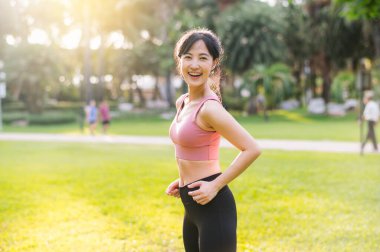 Mutlu bir Asyalı kadın olarak yaşamanın mutluluğunu yaşayın. 30 'lu yaşlarda, gün batımında parkta kameraya gülümserken. Sağlıklı ve hayat dolu bir yaşam tarzını benimse.