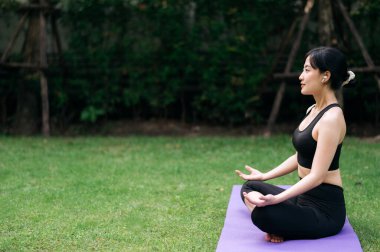 Orman Yogası Akışı. Yeşilliklerin ortasında, 30 'lu yaşlarda Asyalı kadın spor kıyafetleri giyiyor doğayı ve pratiği harmanlıyor, refahı, rahatlığı ve canlılığı kucaklıyor..