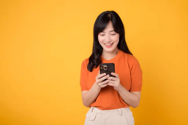 Uśmiechnięta Azjatka Trzydziestce Pomocą Smartfona Ubrana Pomarańczową Koszulę Żywym Żółtym — Zdjęcie stockowe