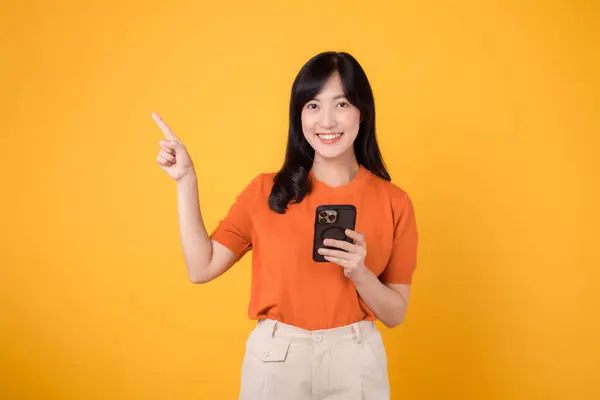 Uśmiechnięta Azjatka Trzydziestce Ubrana Pomarańczową Koszulę Używająca Smartfona Wskazująca Wolne — Zdjęcie stockowe