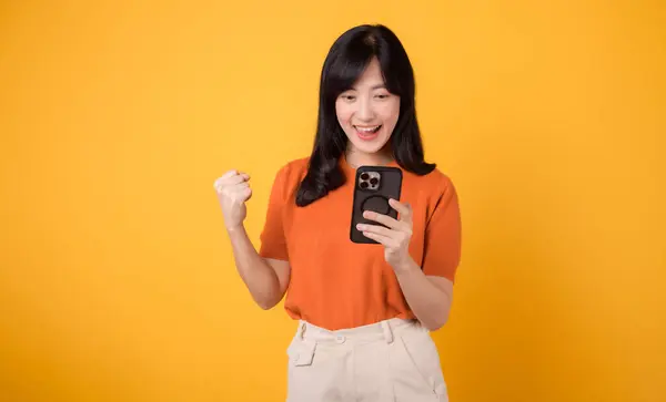 Fröhliche Asiatin Die Orangefarbenes Hemd Smartphone Mit Erhobener Faust Auf — Stockfoto