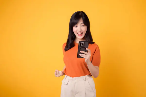 Lächelnde Asiatin Die Orangefarbenes Hemd Smartphone Mit Erhobener Faust Auf — Stockfoto