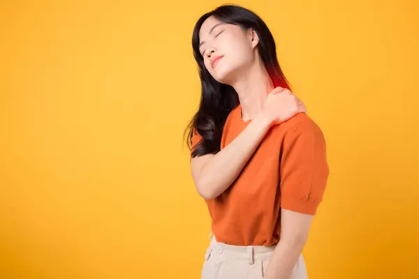 若いアジアの女性 30S 首の筋肉の肩の痛みの損傷を黄色い背景で隔離したオレンジ色のシャツを身に着けている女性人 頭痛療法の医学のオフィスの症候群の概念をチェックして下さい — ストック写真