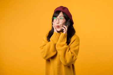 Modayı takip eden bereli ve sarı kazaklı bir kadın model, canlı sarı bir arka planda akıllı telefonuyla konuşurken neşesini dile getiriyor..