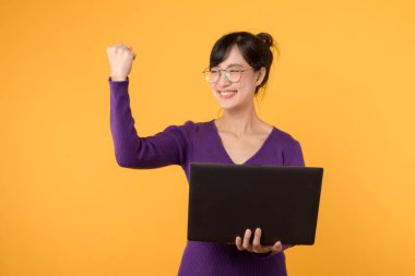 Bilgisayarı ve yumruğu havada çekici bir iş kadını dijital girişimciliği ve ofisinde başarıyı sembolize ediyor. Sarı arka planda mor gömlek ve gözlük takıyor..