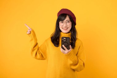 Modern iletişim. Kırmızı bereli ve sarı kazaklı genç bir kadın, akıllı telefonunu neşeli bir internet ortamında kullanıyor..