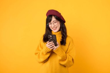 Sarı kazak giyen genç, güzel Asyalı bir kadın ve kırmızı bereli bir kadın akıllı telefon kullanarak dünyayı keşfederken mutlu oluyorlar. mobil uygulama kavramı.