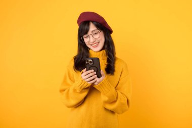 Sarı kazak giyen genç, güzel Asyalı bir kadın ve kırmızı bereli bir kadın akıllı telefon kullanarak dünyayı keşfederken mutlu oluyorlar. mobil uygulama kavramı.