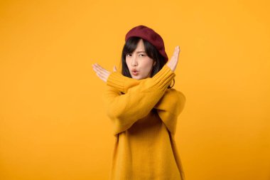 30 'lu yaşlarda, sarı kazaklı ve kırmızı bereli genç bir Asyalı kadın, canlı sarı bir arkaplana karşı sert bir ret hareketi yapıyor..