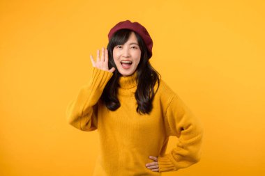 30 'lu yaşlardaki kendine güvenen genç Asyalı kadın, sarı bir süveter ve kırmızı bereyle şık bir duyuru yapıyor..