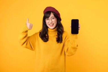 Japon, Koreli ve Çinli etnik kökenler birleşmiş, kırmızı bere ve gözlük takmış, parlak sarı bir arka plana karşı akıllı telefon kullanırken başparmaklarını gösteriyorlar..