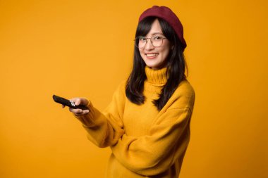 30 'lu yaşlarında, sarı bir kazak giyen rahat genç bir kadın elinde uzaktan kumandayla sinemayı seviyor. sarı arkaplan.