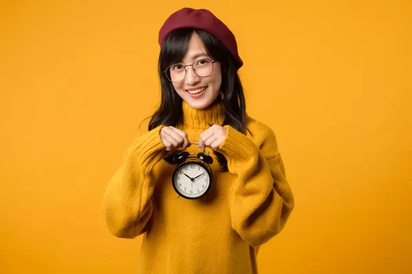 아시아의 노란색 스웨터와 빨간색 베레를 그녀는 활기찬 노란색 배경에 시계를 스톡 이미지