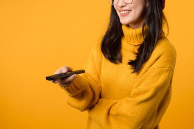 Sarı kazak giymiş, uzaktan kumandayla televizyonu çalıştırırken gülümseyen genç Asyalı kadını yakından çek..